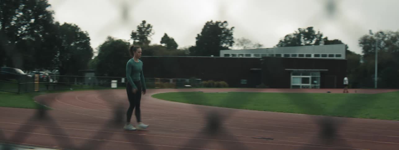 A woman is on a red running track and she is walking fast and bouncing