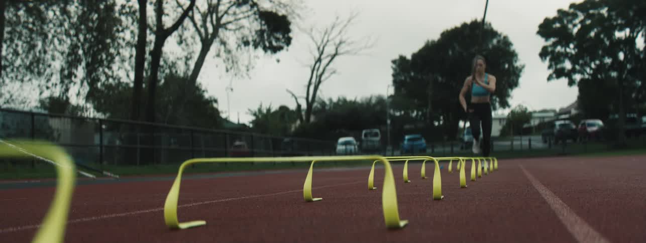 A woman jumps over short hurdles while holding a pole in her hand