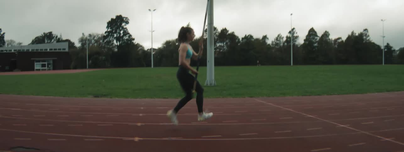 A young woman jogs with a pole on a track prepping for a vault under cloudy skies