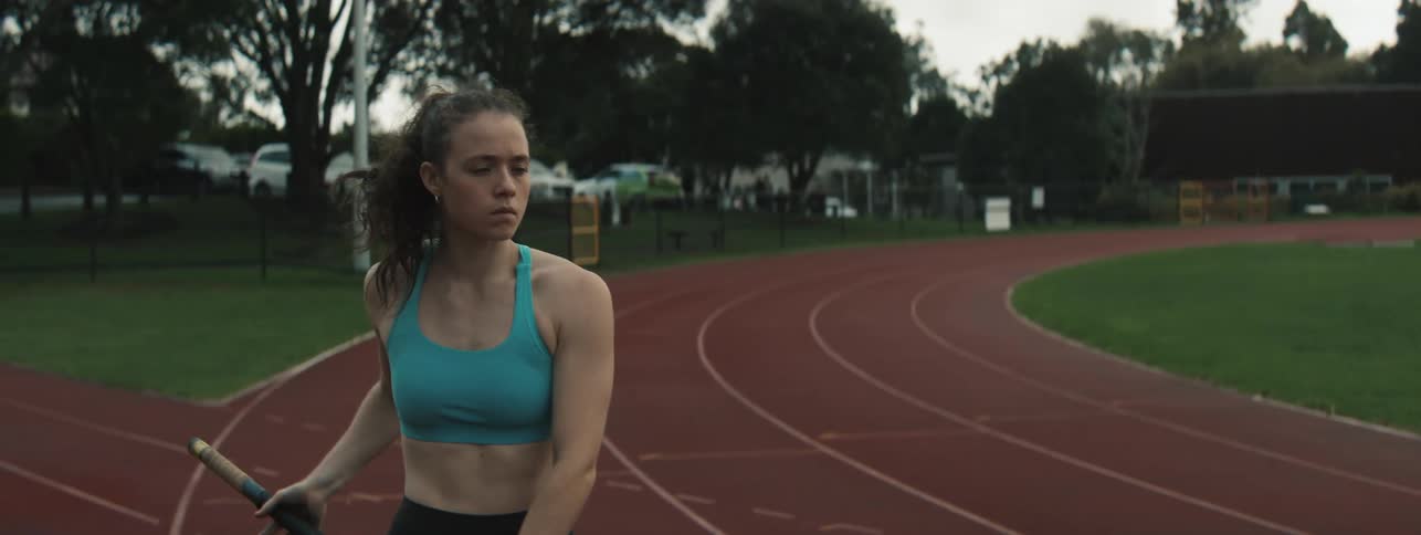 A female athlete prepares for a pole vault on a red running track