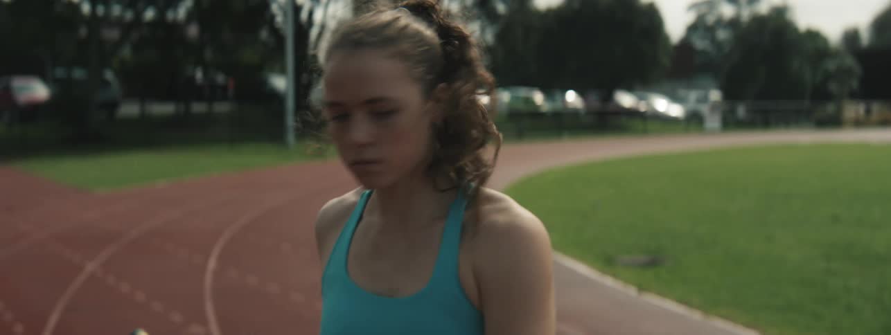 A young woman holds a vaulting pole on a running track focuses and starts running