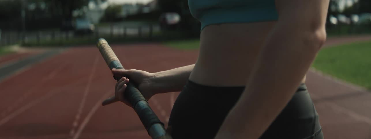 Female pole vaulter grasps a pole while standing on a running track on a summer day