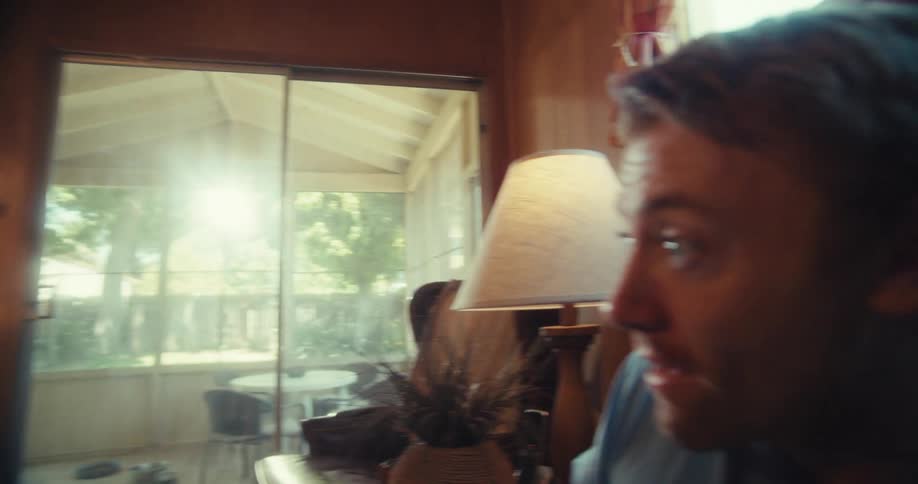 An elderly man plays vr as his son watches smiling in a cozy living room