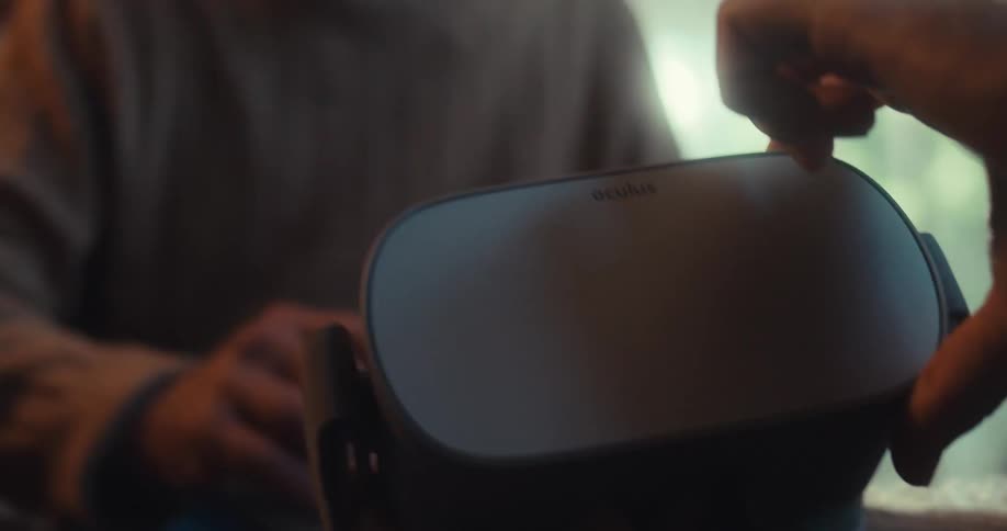 An elderly man watches another man explain how to use the virtual reality headset in front of them