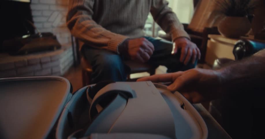 An old man sits nearby as another person flips open a case of a vr headset