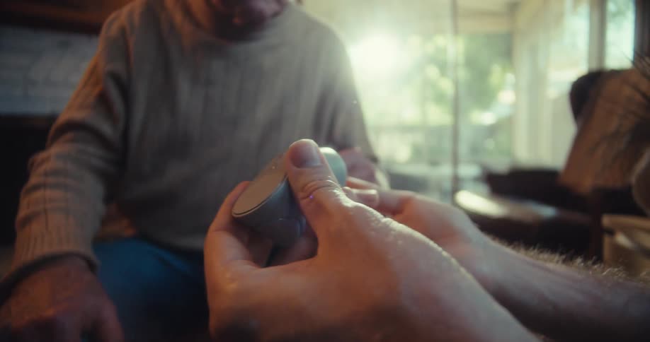 Man shows a virtual reality controller to an elderly man while they sit in the living room