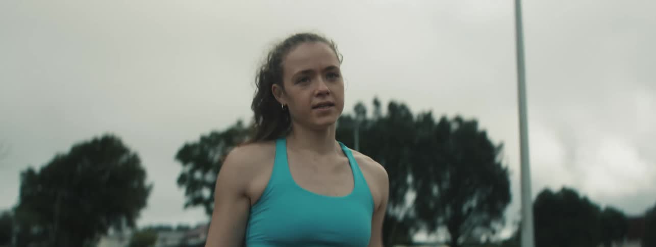 A female athlete runs on a track while jumping over mini hurdles with a pole in hand