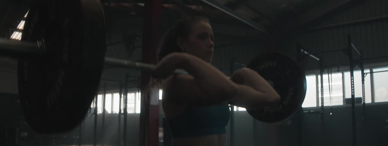 Female athlete standing in a gym lifts a heavy weight bar