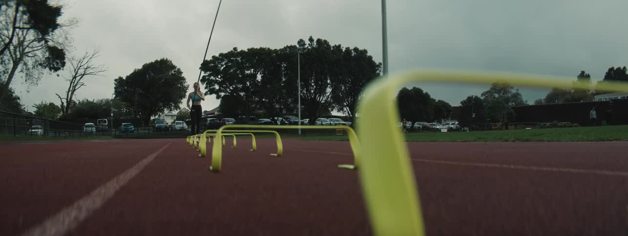A female athlete runs towards the camera jumping over yellow mini hurdles on a red outdoor track