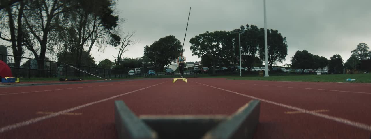 A woman runs down a track with a pole in her hand and then stops and walks back to the start