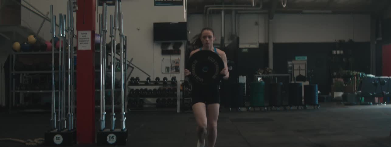 Woman exercising running through a gym with a weight plate