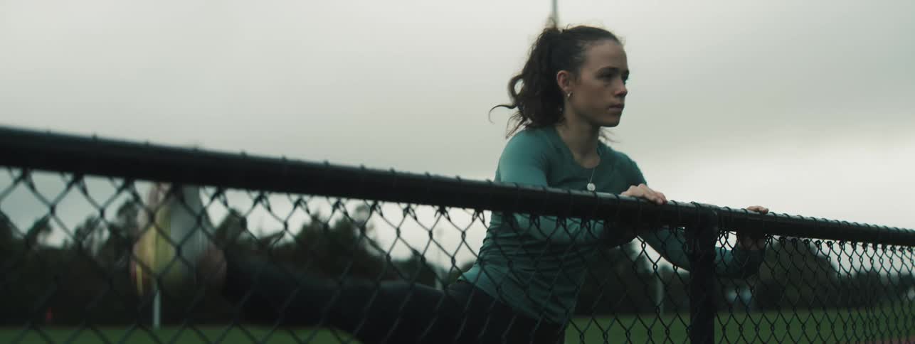 The woman is holding on to the fence while kicking her leg