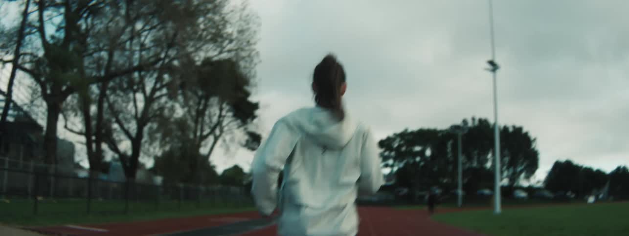 Woman wearing a hoodie exercises on a running track under an overcast sky