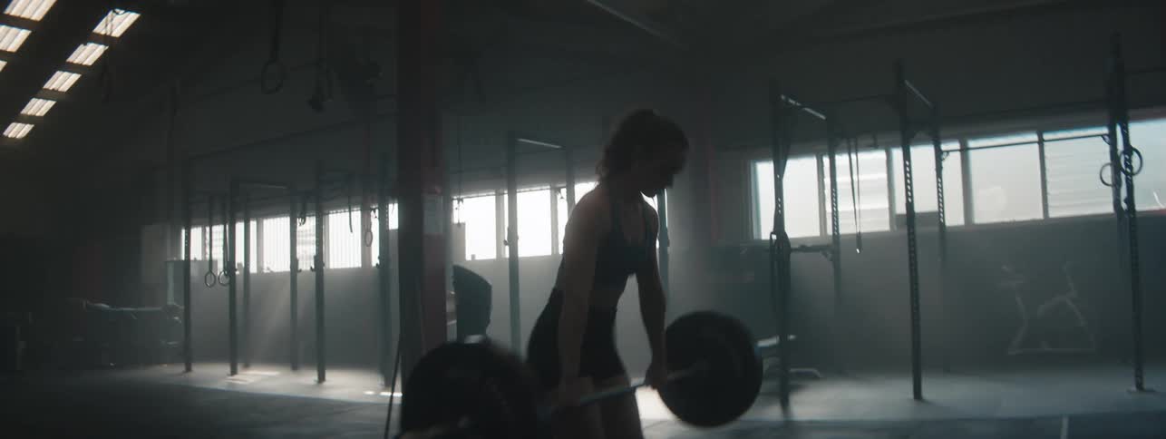Concentrated woman doing weightlifting with a free barbell in a gym