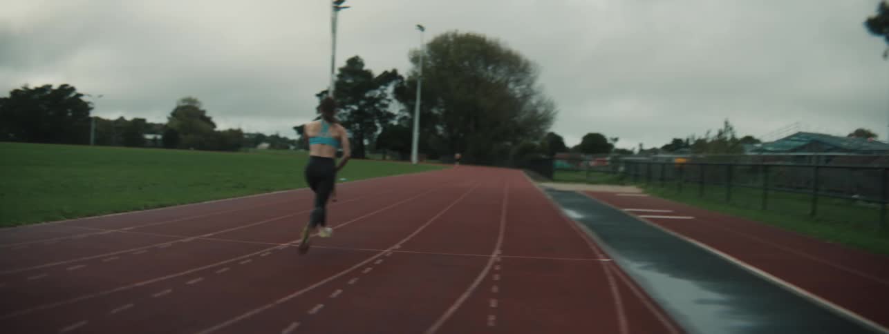 Pole vaulter practices by running down a track in daytime while carrying a pole in the air