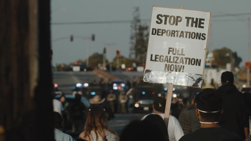 Police stand and watch while a crowd protests deportations and asks for full legalization