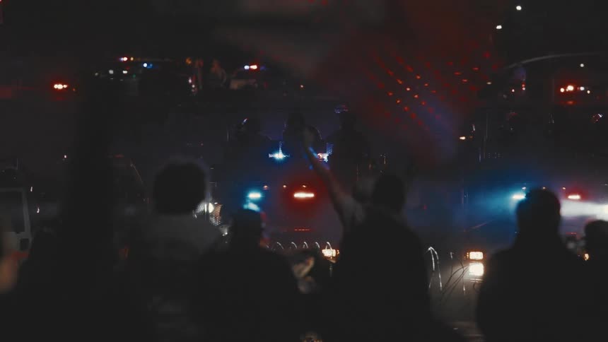 Protesters wave mexican flags while the police stand among their police cars at an intersection at night