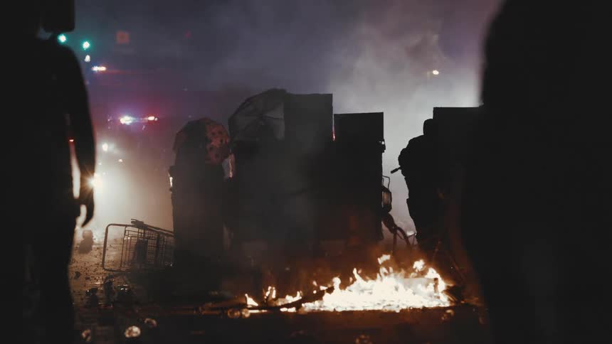 Rioters walk towards the police barricade and flames