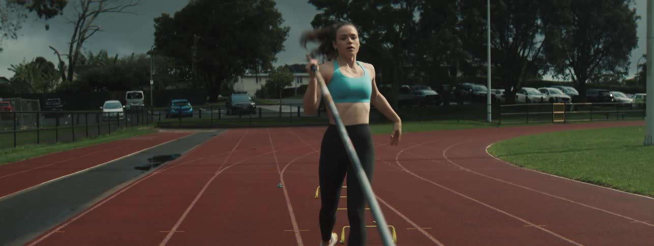 Female vaulter practices on a running track under a stormy sky