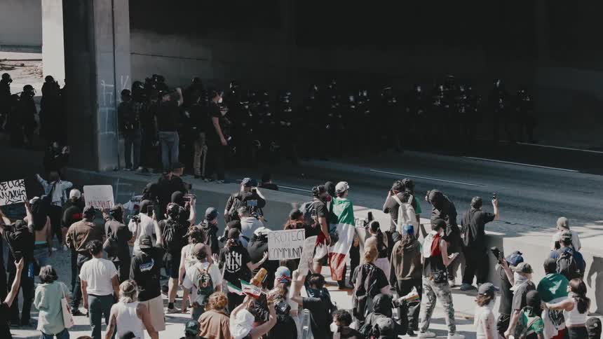 A confrontation between a large group of riot police in tactical gear and a crowd of civilians in an urban setting