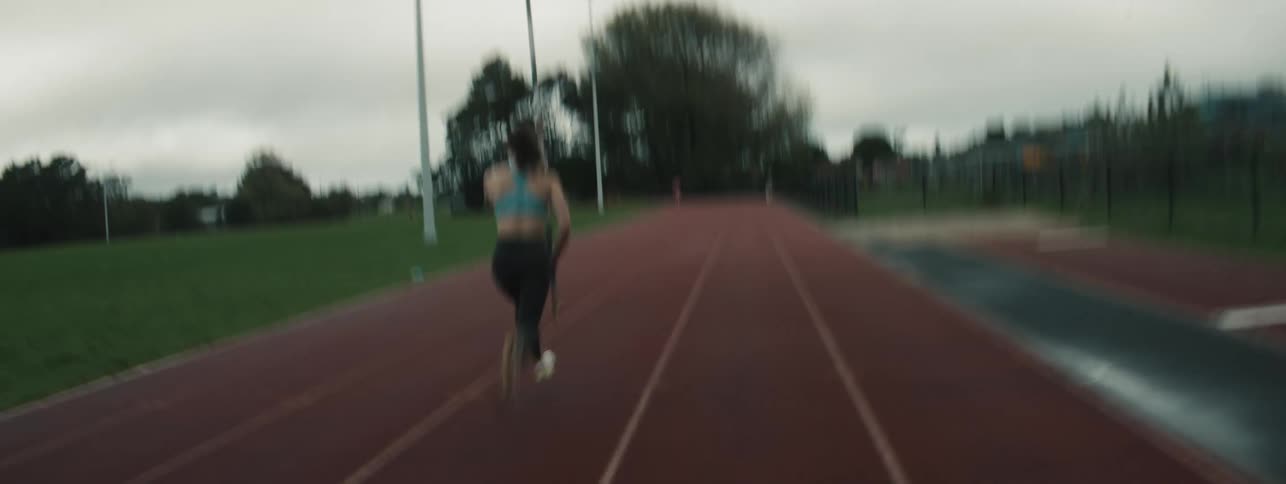 Female athlete runs down a track carrying a pole as she practises for pole vault during daytime
