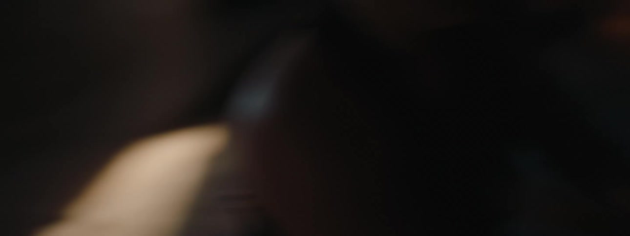 A woman is quickly beating a drum in a completely dark indoor environment with some lights passing through the room