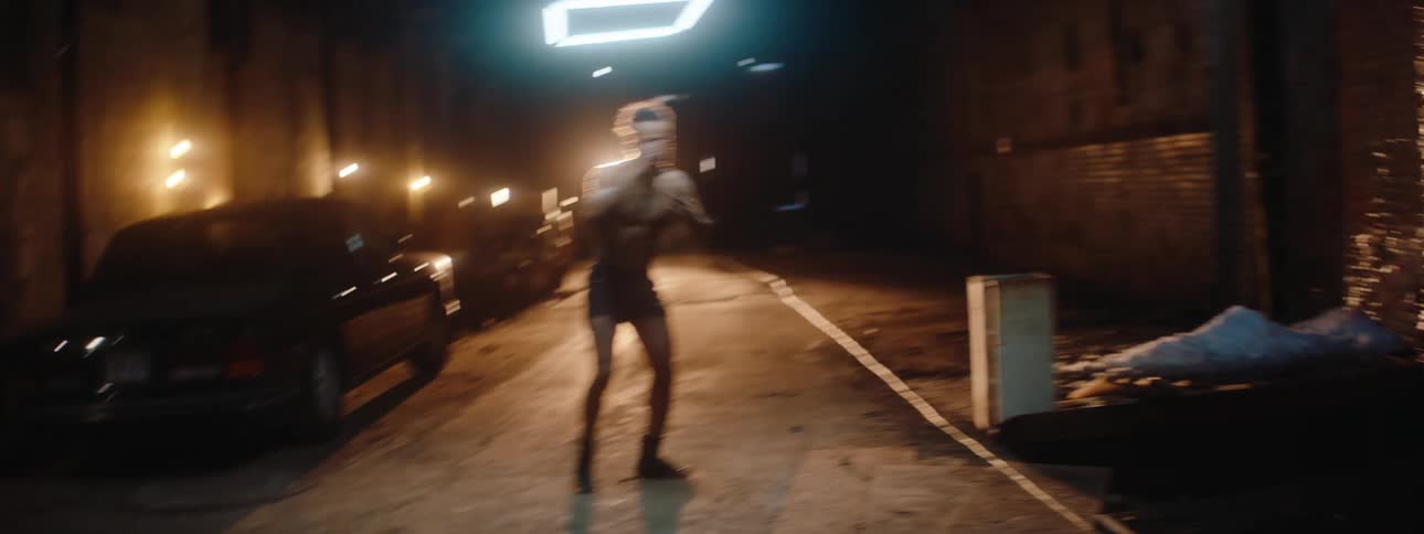 A man pretends to fight by punching and kicking the air in an alleyway at night