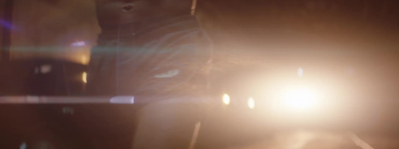 Man practices kickboxing while in a structure lit by the headlights of a parked car