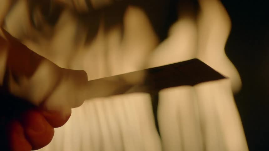 A hand holds a card as flames burn around and behind it