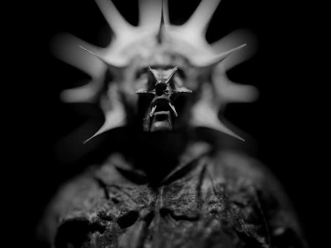 A statue with thorns protruding from its face and an anguished expression is dramatically lit against a dark background