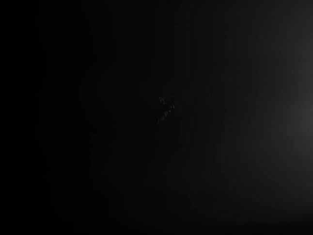 A person floats amid streaks of smoke or fog swept by wind in a dark obscure setting