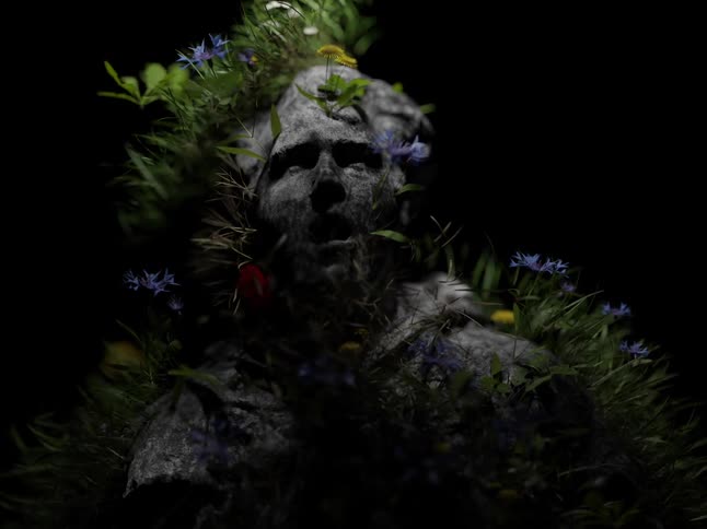 Wind blows the grass and flowers on the statue of a man