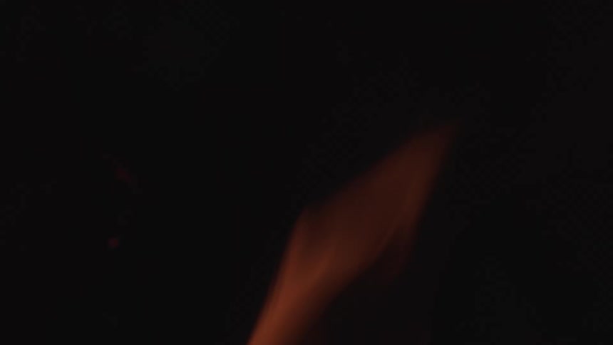 A blurry extreme closeup captures the soft flickering movement of orange flames from a fire against a dark background