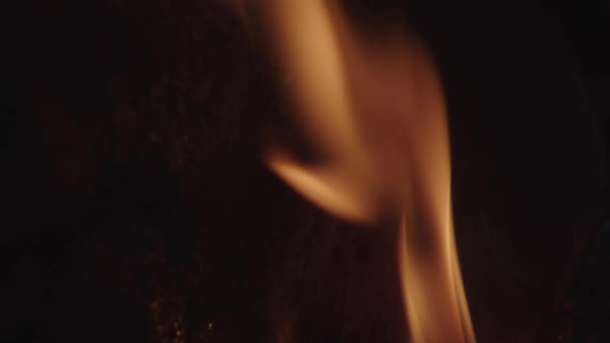 A fire is burning some wood on the ground at night