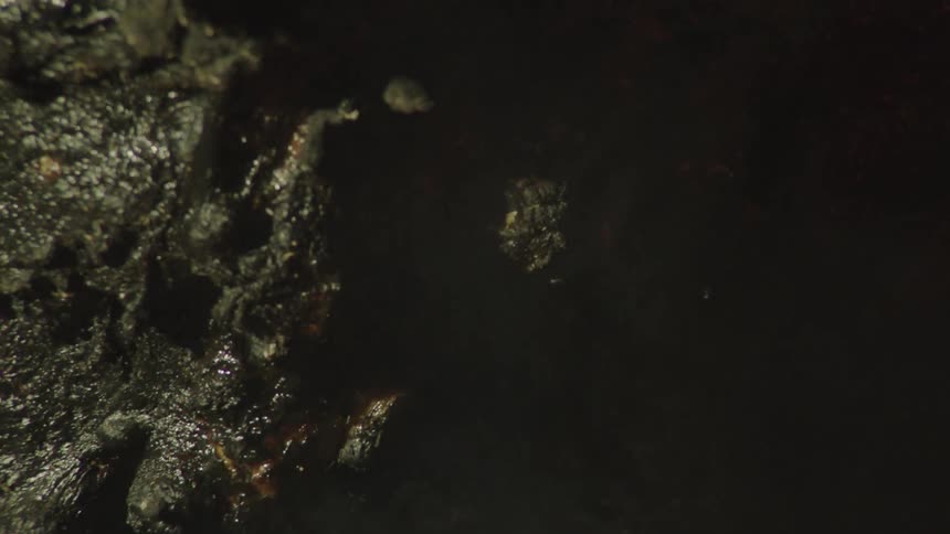 The surface of a stone that is wet and several small drops of water are passing over its surface and it is being hit by a shadow