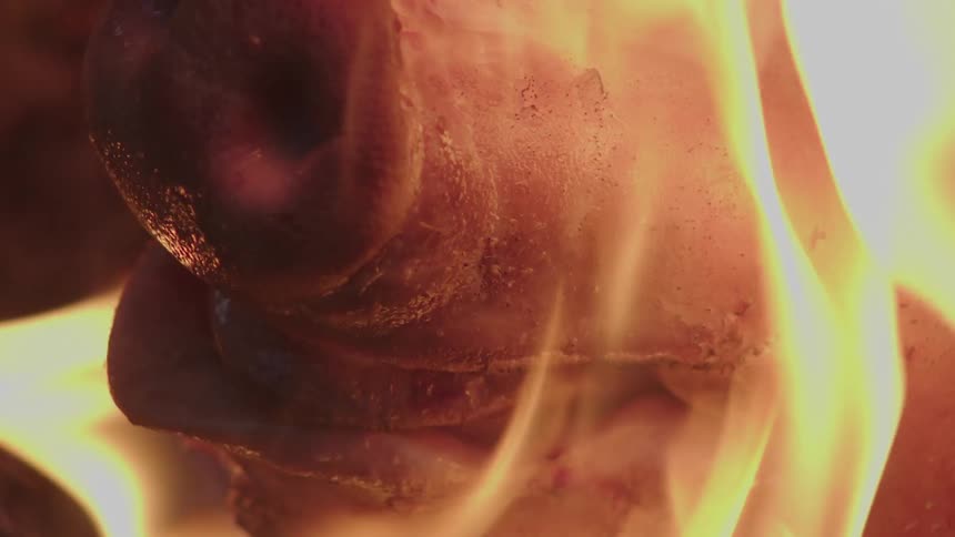 Close up of a pig snout engulfed in flames casting intense orange light against the dark smoky backdrop