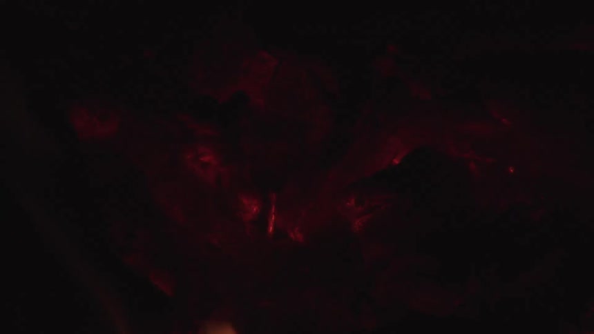Flames lick over a large piece of meat cooking in a fire