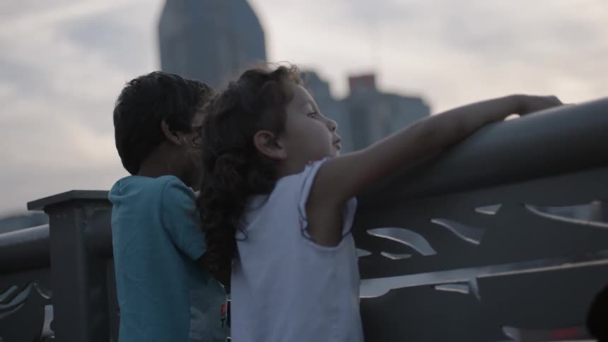 Two children look over a railing at a city