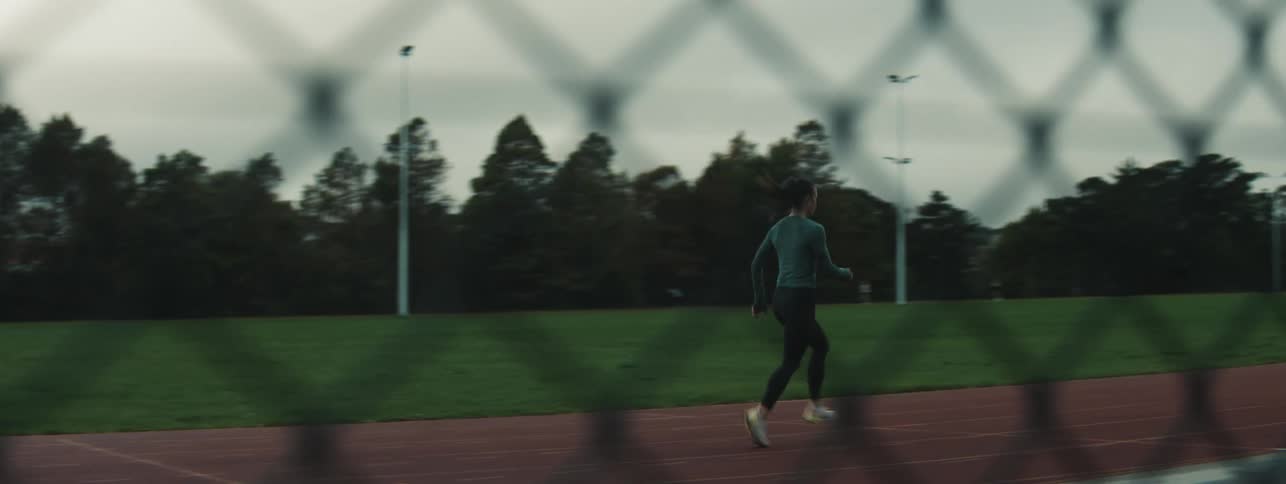 A woman jogs alone on an outdoor track as part of a warmup on an overcast day