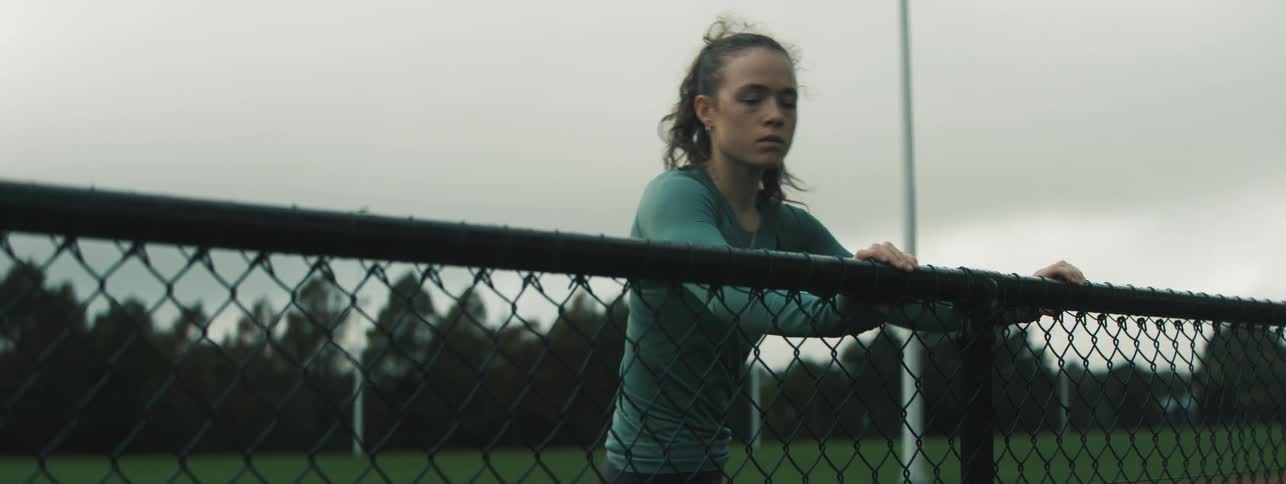 A woman is stretching her legs near a fenced in area