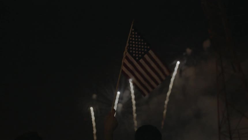 A person waves a flag as they watch fireworks