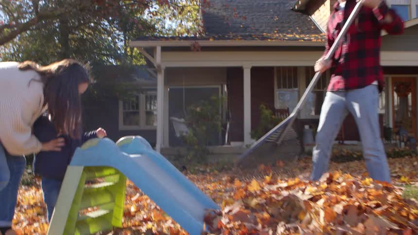 Family having fun with a small child in a yard with dry leaves