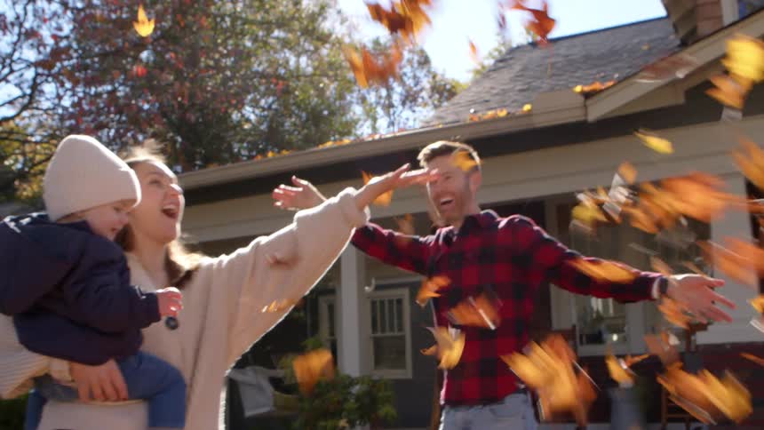 A joyful family plays with autumn leaves in their suburban yard
