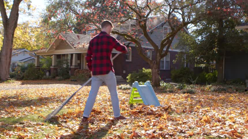 Man raking fall leaves in front yard as wife watches