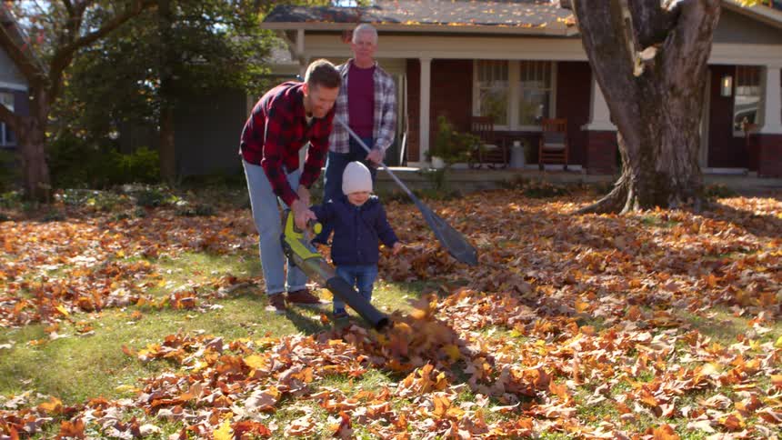 A father is helping his young son use a leaf blower