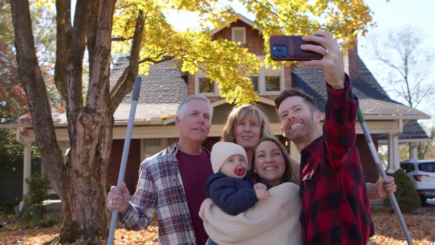 Young dad taking a selfie with his family in front of large tree with fall leaves