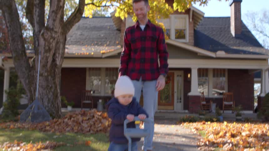 A baby wearing a white hat runs across a leafstrewn lawn accompanied by three adults
