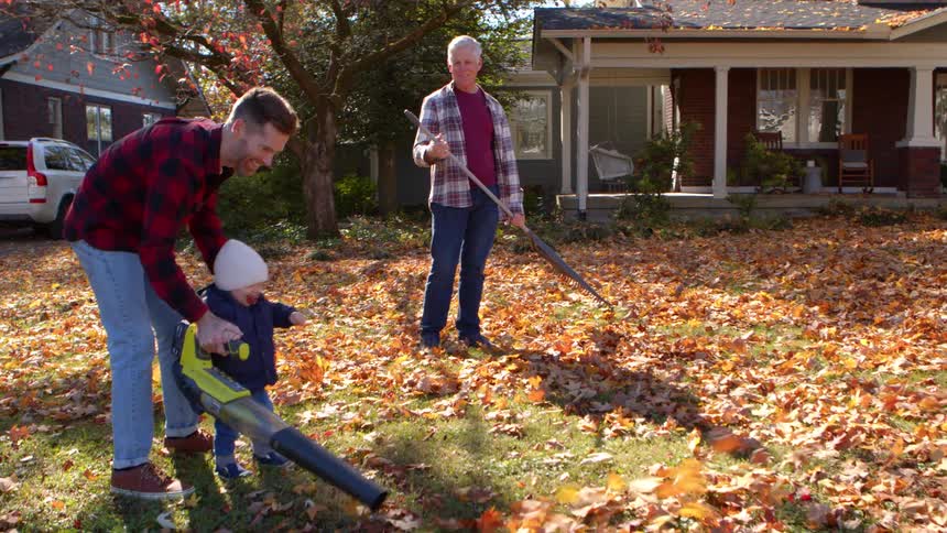 Father with little son and grandfather cleaning the yard in dry leaves