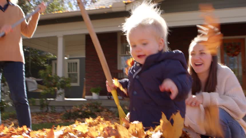 A toddler and his family are outside in the fall playing in a pile of dead leaves