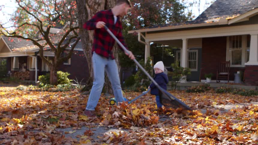 Father cleaning the yard with a young son with a toy next to him